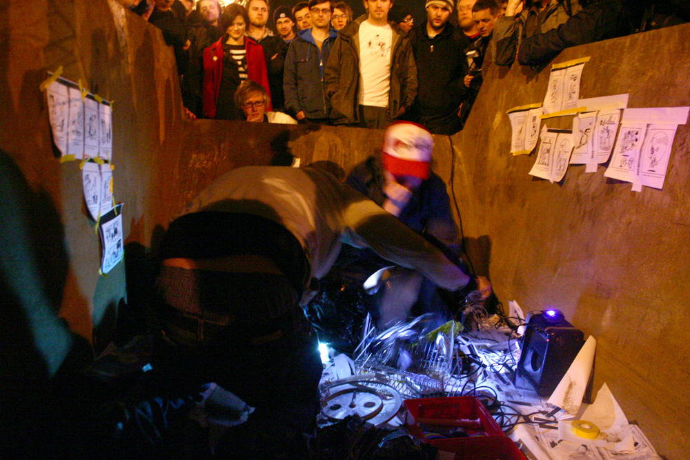 Two members of Usurper in a skip perform whilst audience overlooks