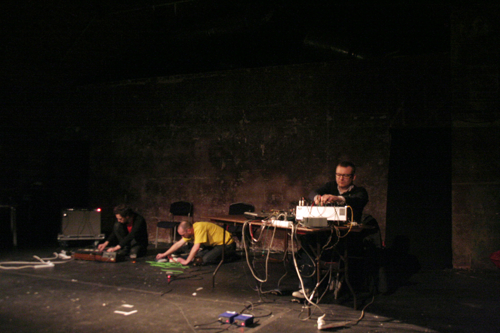 Three men operating electronic equipment. Fraser is in yellow on the floor