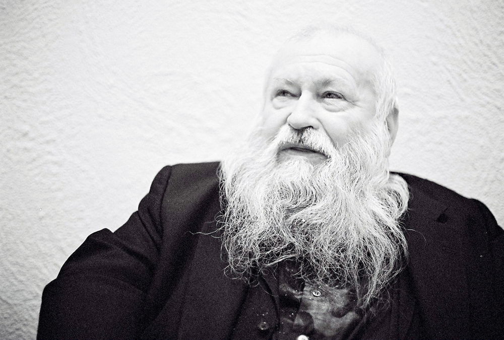 A bearded Hermann Nitsch sits back in a chair looking sideways