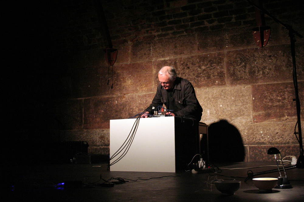 Rolf Julius leans forward over a large white box and mixer and performs