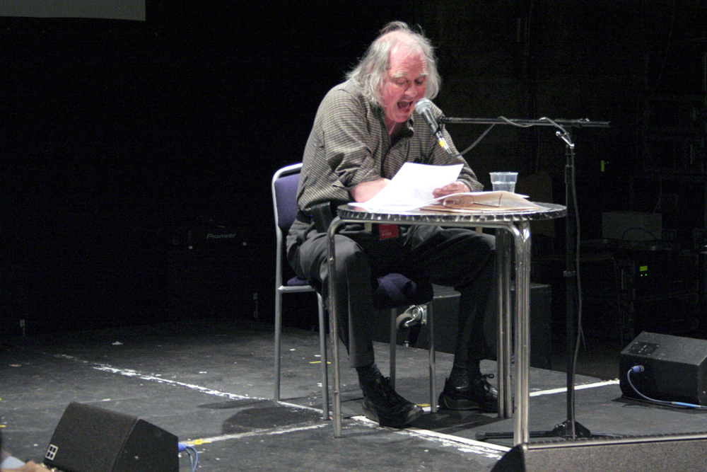 Steve McCaffery sits at a round table and reads into a microphone