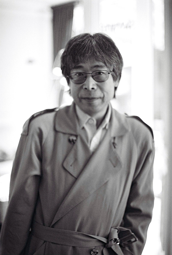Tamio Shiraishi in a mac and glasses poses for a portrait