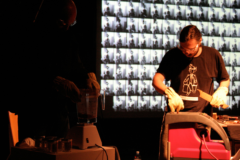 Nikos and Rhordi wood chipping a cello near a projector