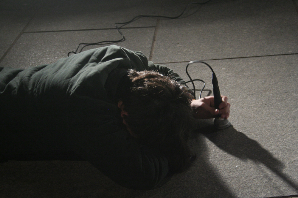Participants lie on the floor outside hitting microphones on the floor