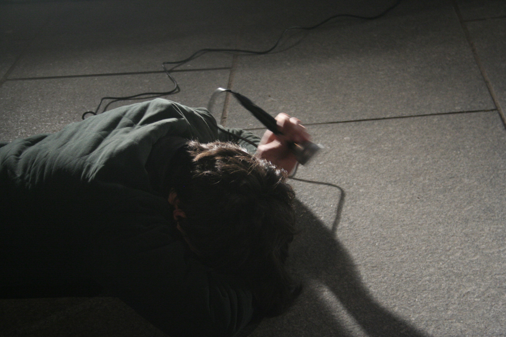 Participants lie on the floor outside hitting microphones on the floor