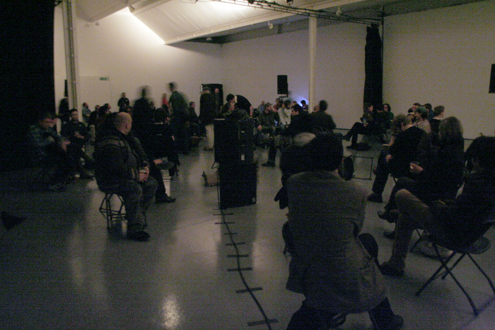 in a dim gallery space people are sat on randomly positioned chairs