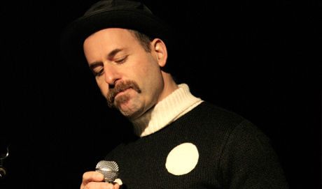 Kenny Goldsmith holds a microphone wearing a white spotted jumper