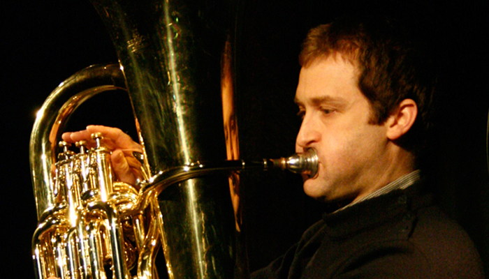 Robin Hayward playing a tuba against a dark background