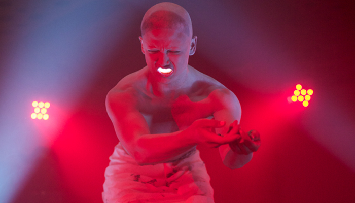 a figure bathed in red writhes as they perform with a red light in their mouth