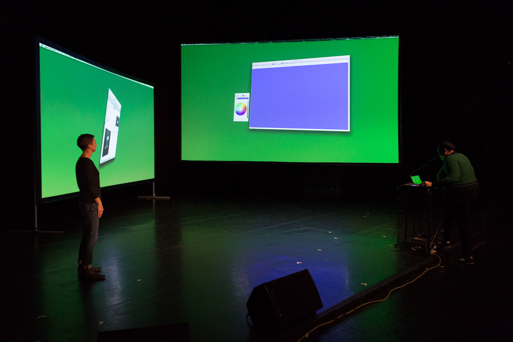 Two large screens glow green on a stage. They are at angles to one another