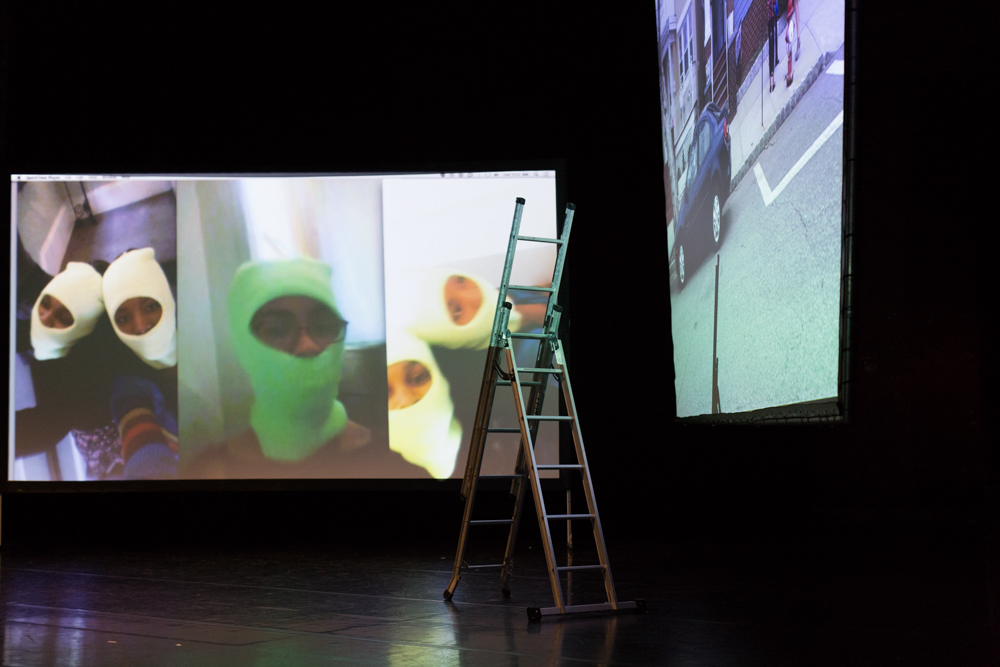 Two large screens on a stage with images of people wearing green balaclava