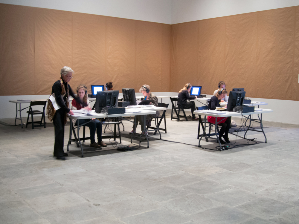 An installation of brown paper covered walls and folks sat at tables of research