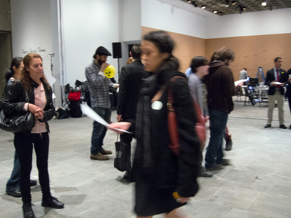 A blurry female figure moves across the frame holding a piece of paper