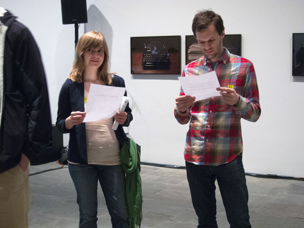 A man in a checked shirt looks down at a piece of paper, as a woman looks around