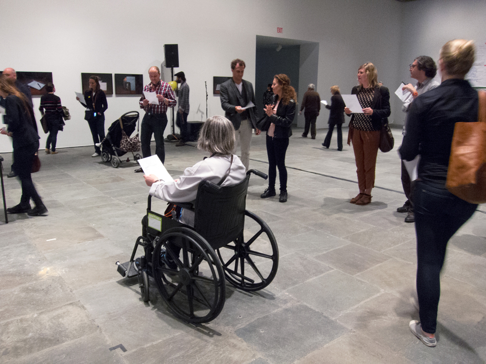 A group of people each holding a sheet of paper walk around each other