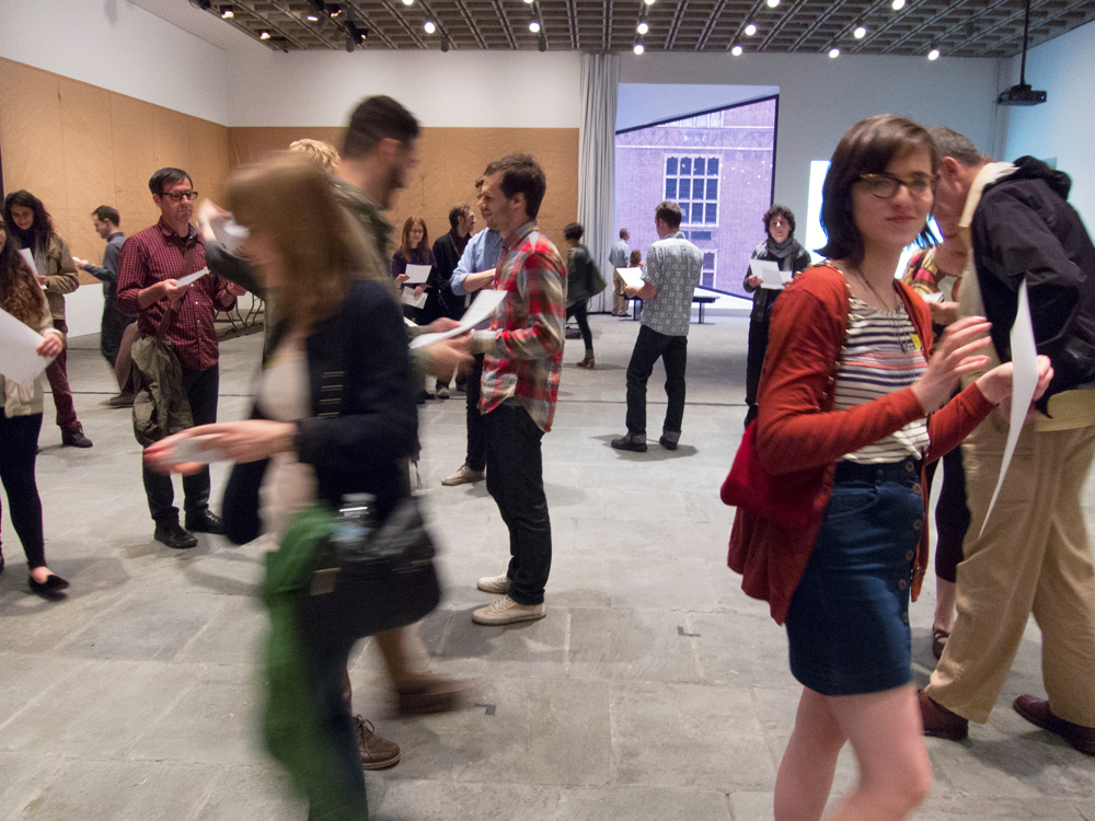 A group of people each holding a sheet of paper walk around each other