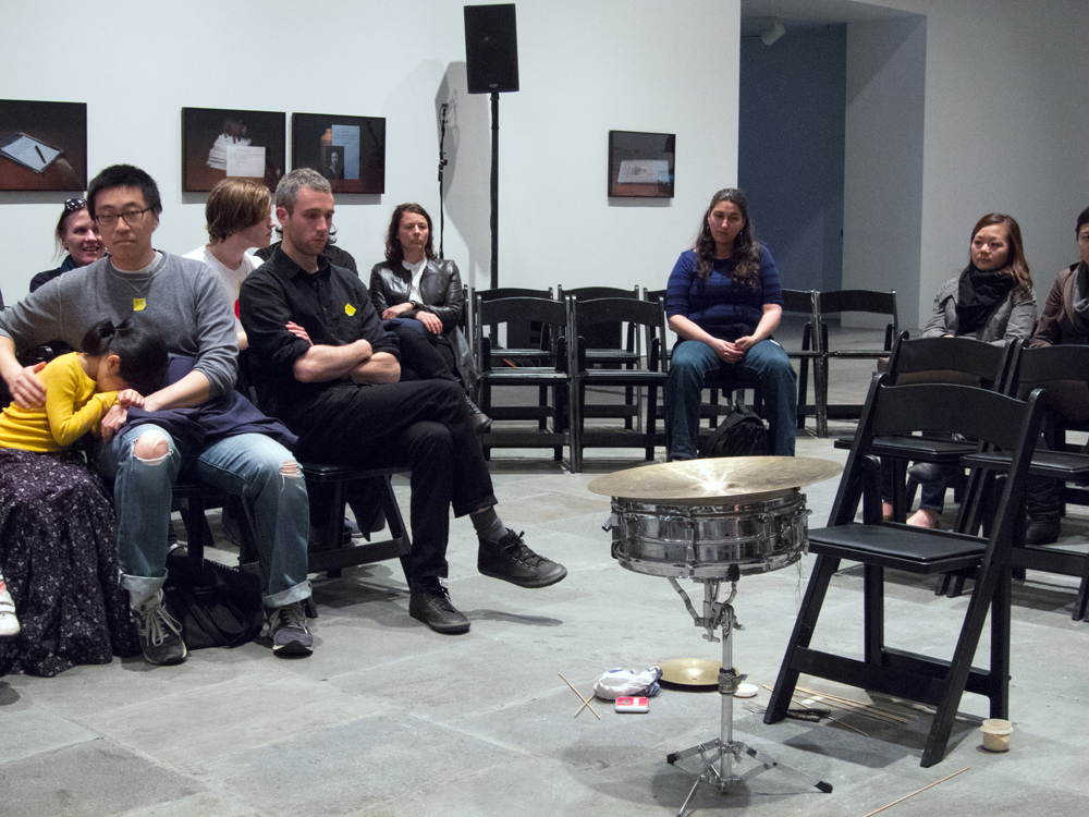 A small audience looking at sean meehan's percussion and chair with no sean