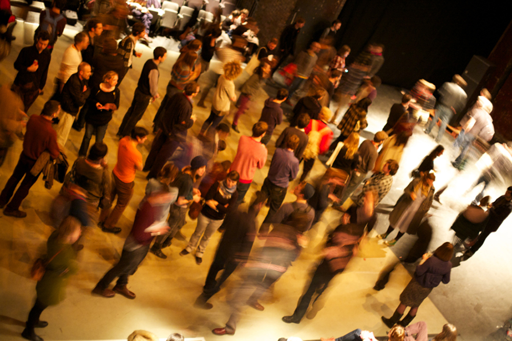 A blurry crowd mill on dance floor in the centre of a theatre space