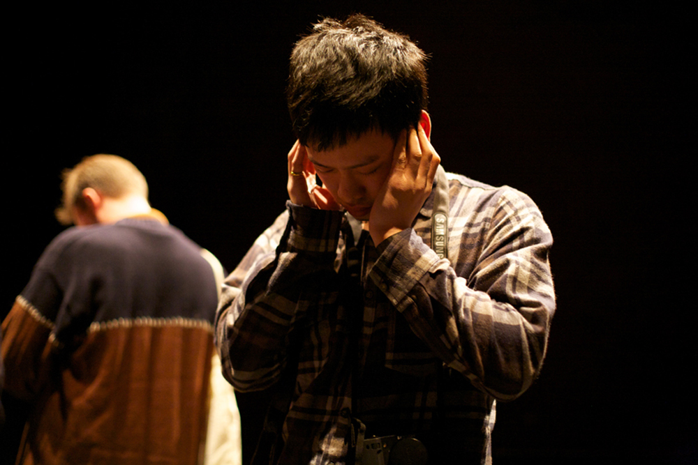 An audience member bows their head with their fingers in their ears