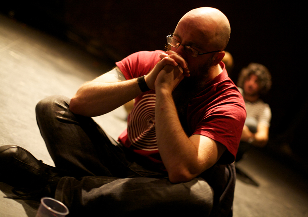 An audience member sits on the floor crossed legged and rests on their hands