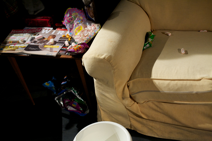 On a table next to a beige sofa there are magazines and flump sweets