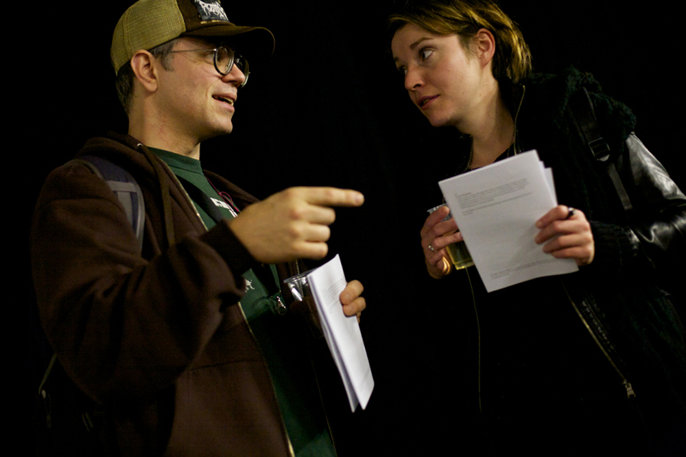 Two people, one in a baseball cap and glasses talk whilst holding handouts