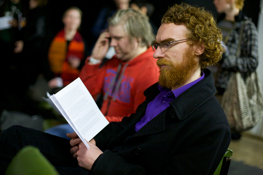 A man with a beard sits and reads a handout
