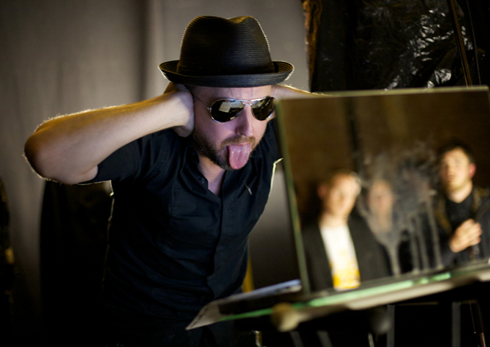 Tim Goldie wearing sunglasses and hat holds his hands over his ears, tongue out