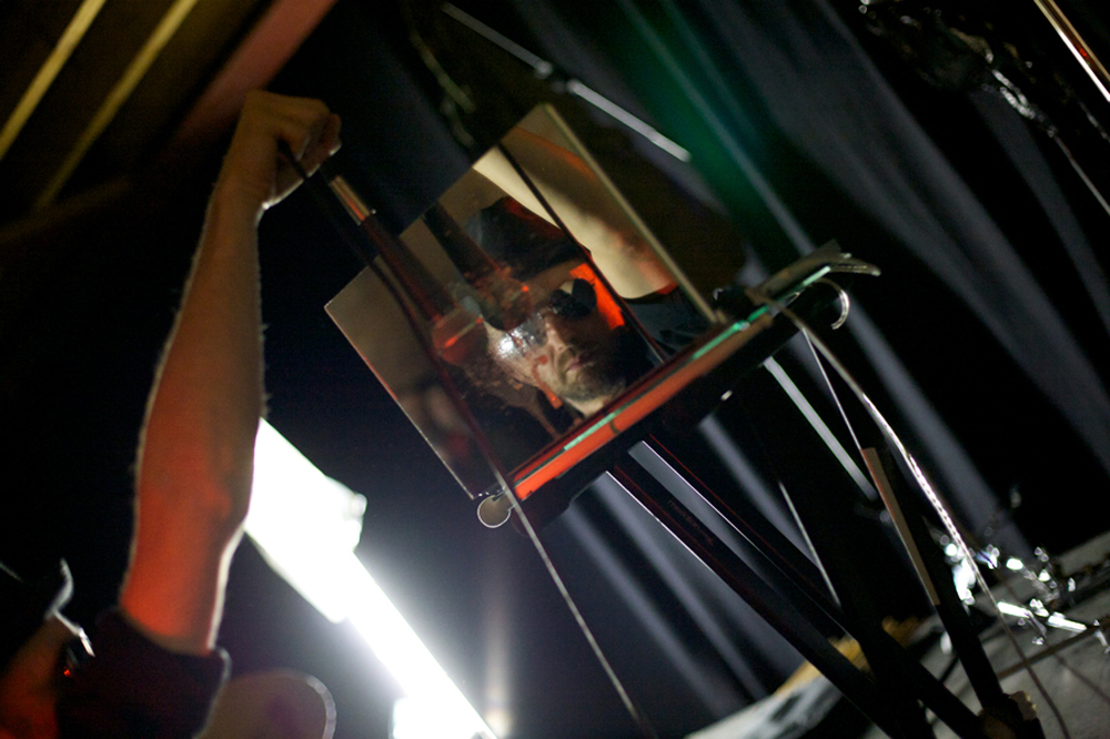 A reflection in a mirrored laptop of Tim Goldie swinging a microphone