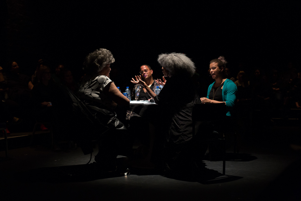 Four people sat around a table on a stage. They are having a discussion.