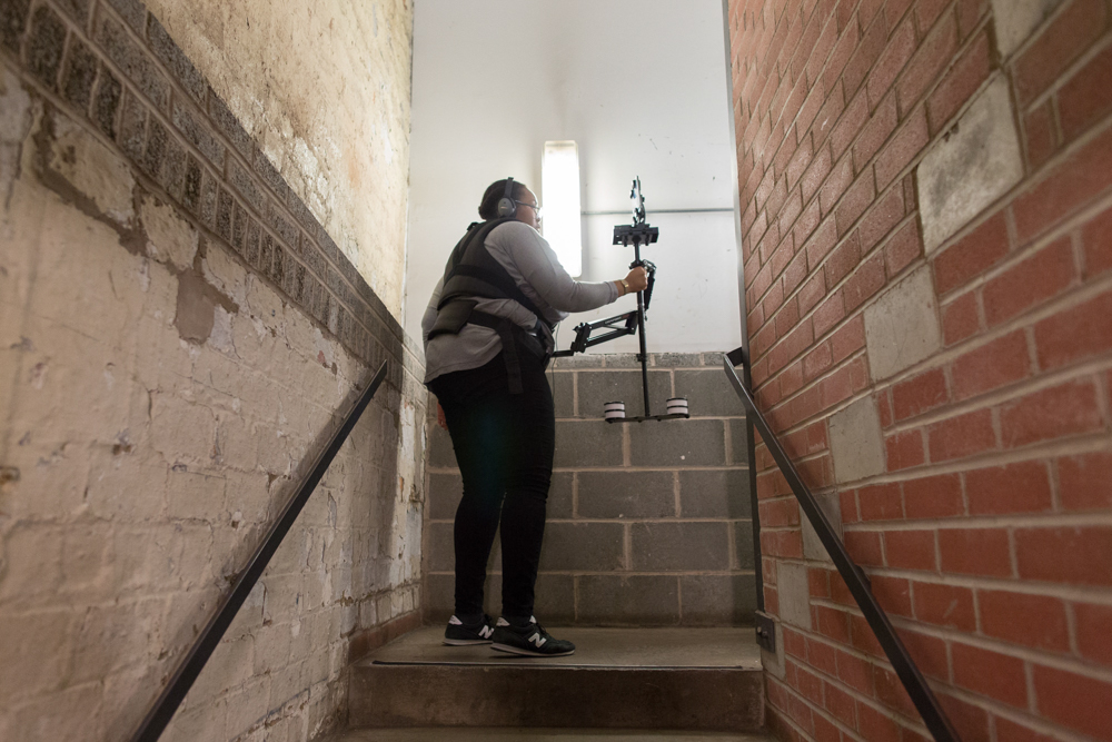 Sondra Perry in a stairwell wearing a Steadicam harness
