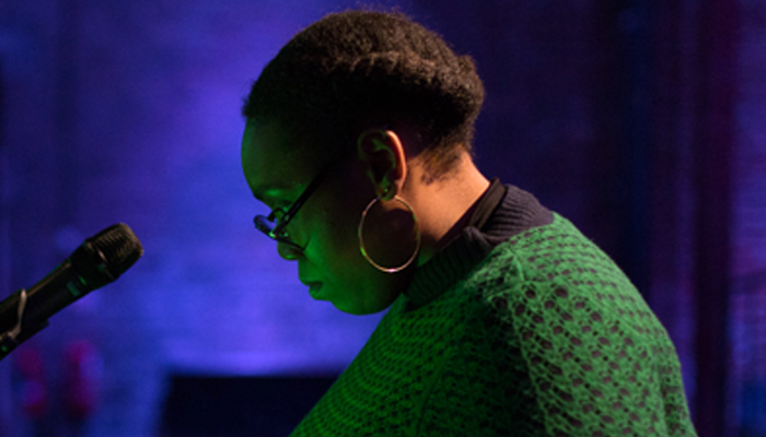 Sondra Perry's face, in profile, is lit in green, the background is blue