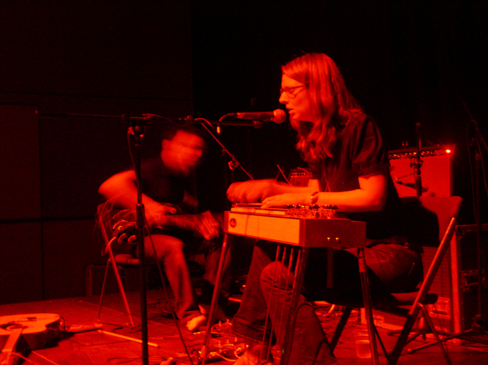 Two people playing electric guitar and lap steel guitar respectively, red light