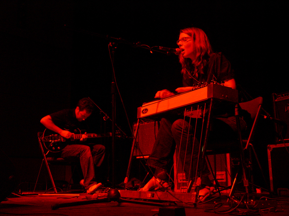 Two people playing electric guitar and lap steel guitar respectively, red light