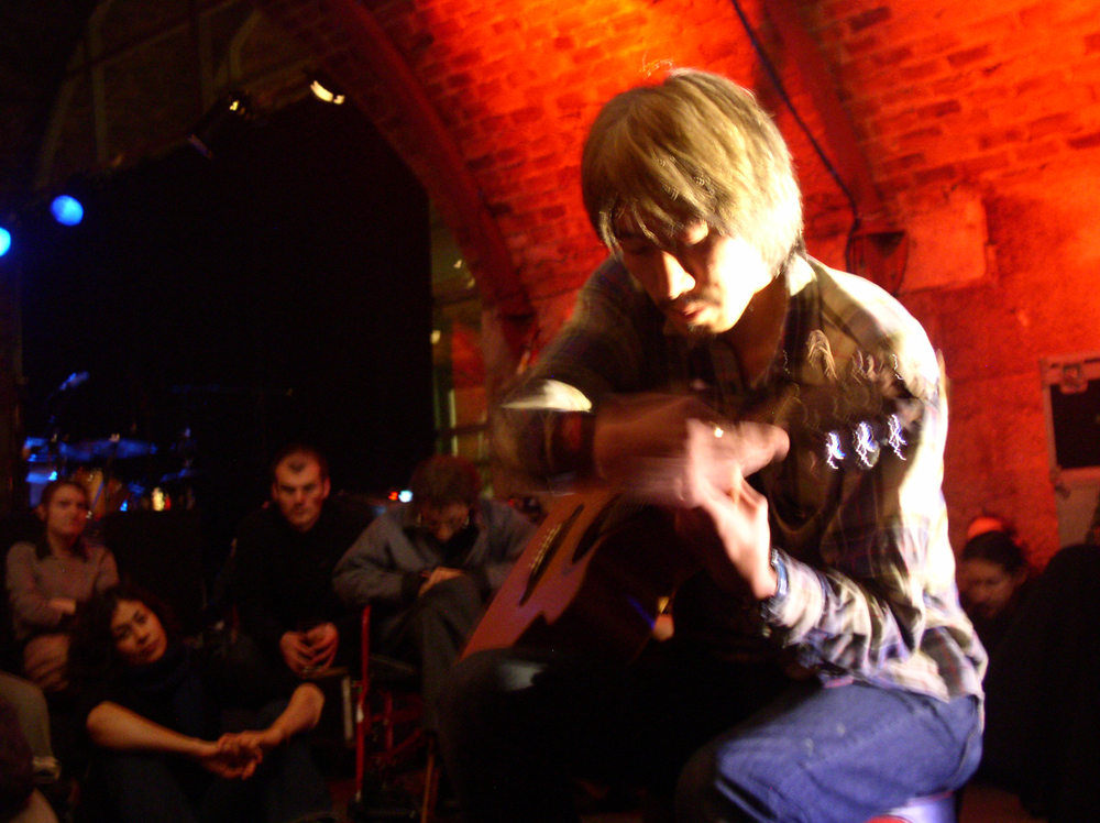 Tetusi Akiyama sitting with a guitar surrounded by audience