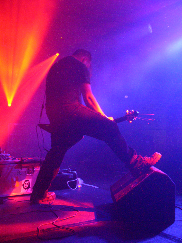 A musician plays a low slung flying v guitar with a foot on a monitor