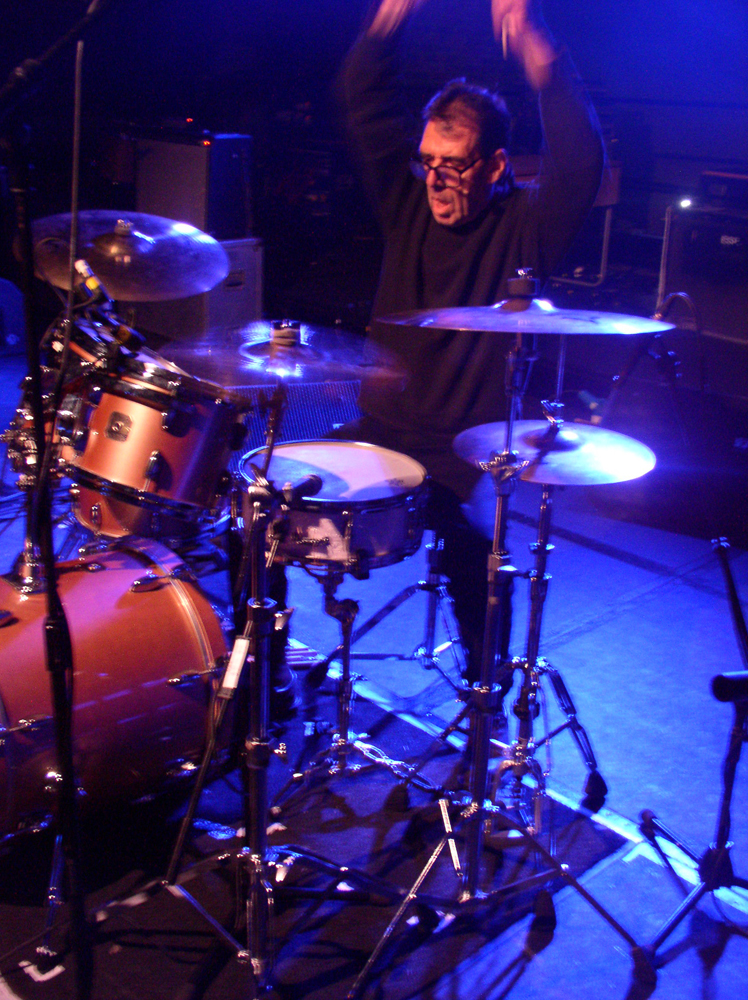 Tom Bruno holds his arms up above a drum kit