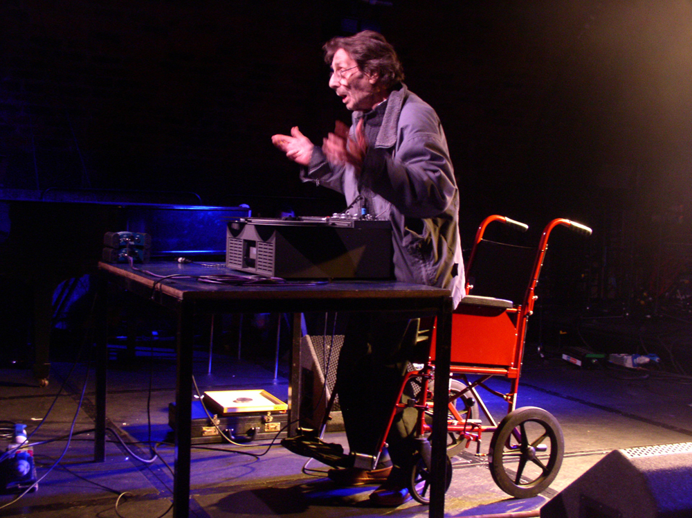 a man stands above a wheel chair gesticulating with his hands