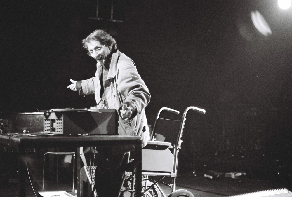 Henri Chopin on stage smiling and operating a tape recorder