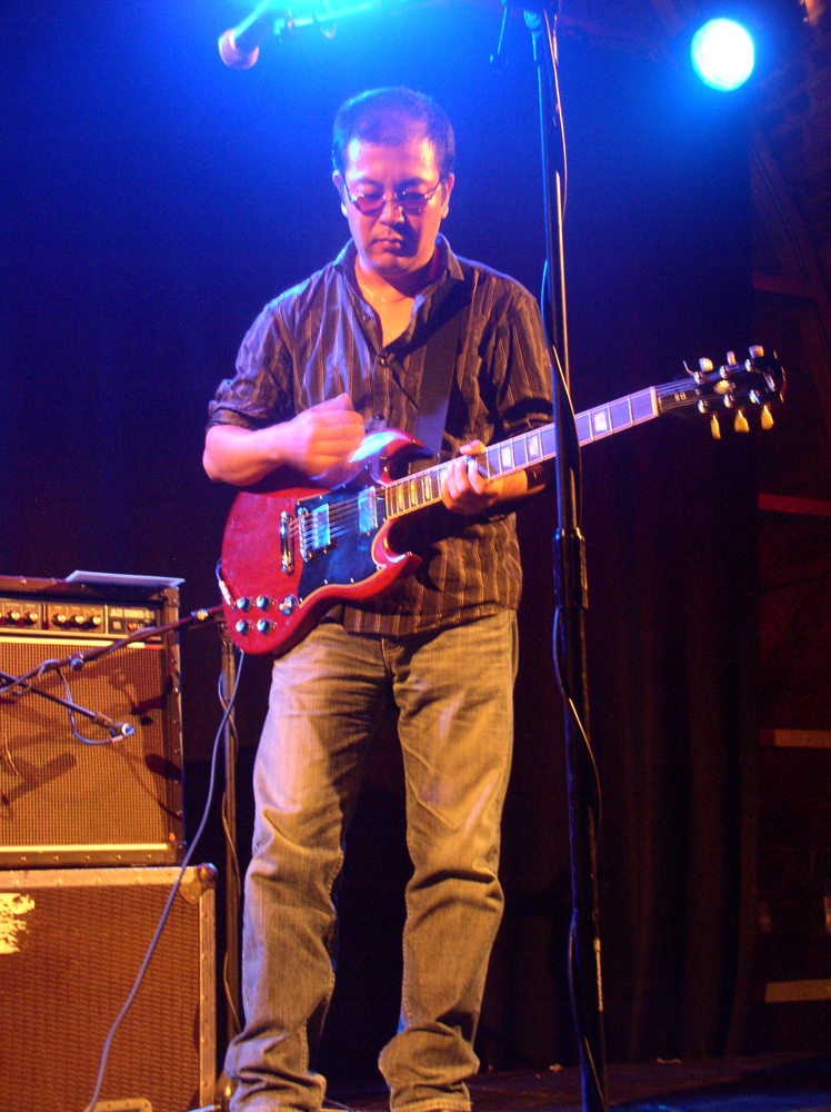 Someone playing a red guitar in a halo of blue light