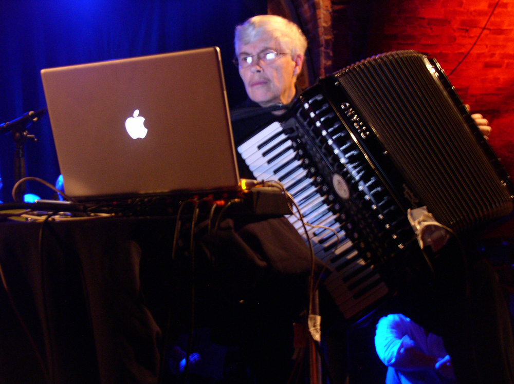 Pauline Oliveros holding an accordion while reading information from a laptop