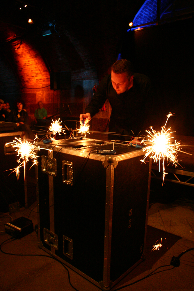 A man with a small beard burns sparklers indoors on a table