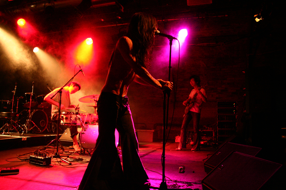 Flared trousers in the foreground, rock trio in pink light 
