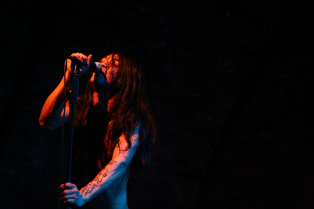 Left of centre man singing into a microphone with tattooed arm below