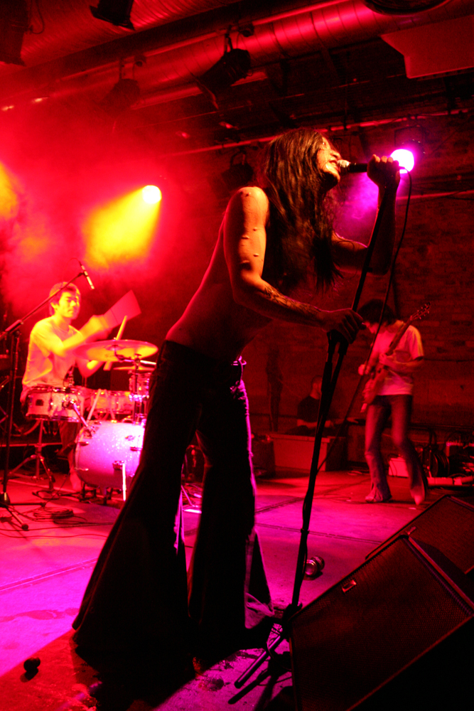 A scarred rock band shot from below with pink light and flared trousers
