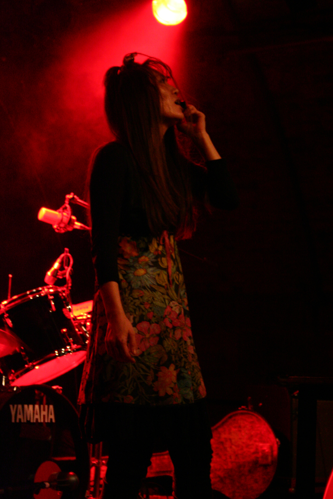 A woman with long hair holds a microphone to her mouth in red light