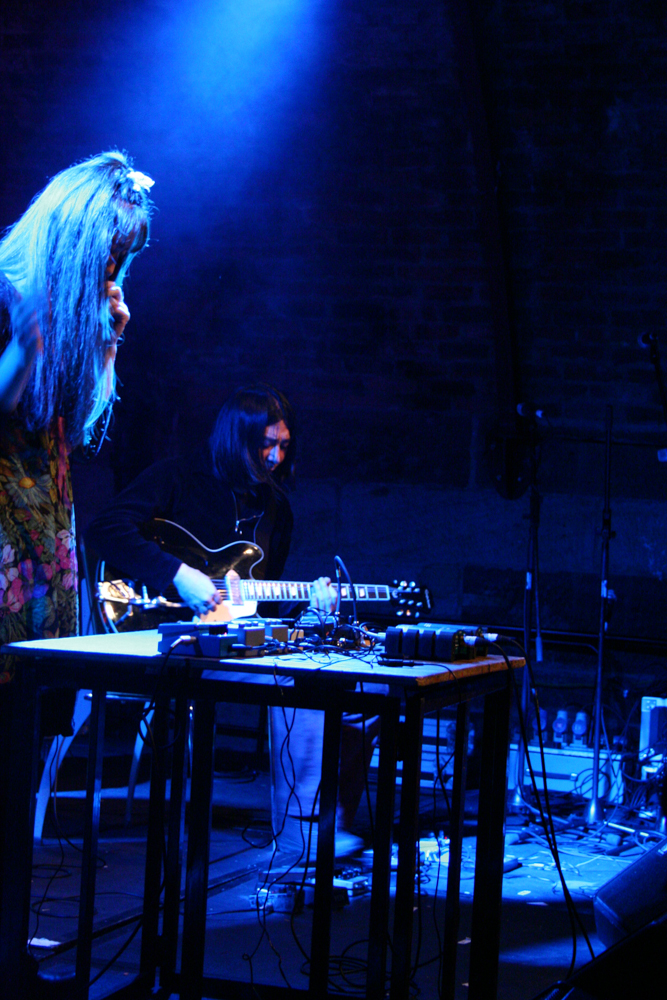 Blue light above a standing woman and a seated guitar playing man