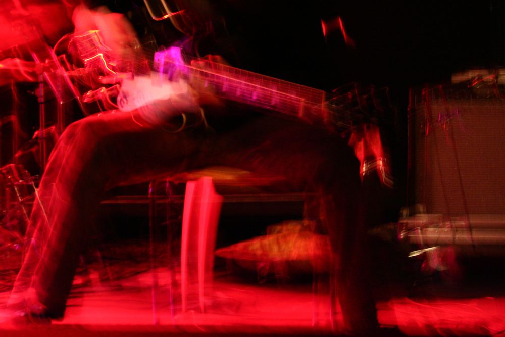 A guitarist moves while performing, a distorted image in pink tones