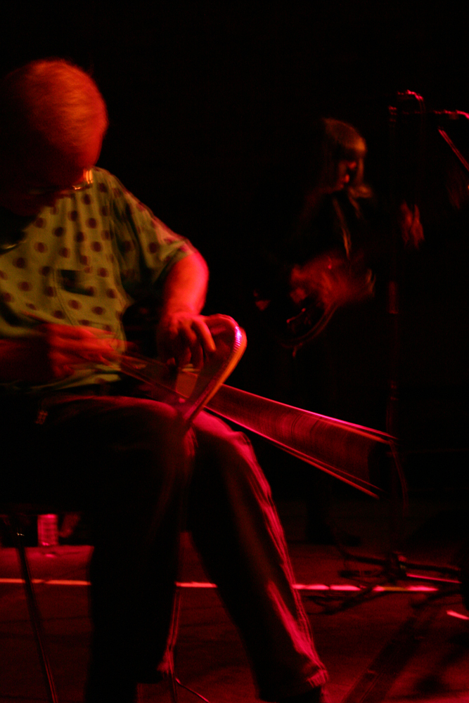 Tony Conrad bowing a torn drum head, Keiji Haino in the background