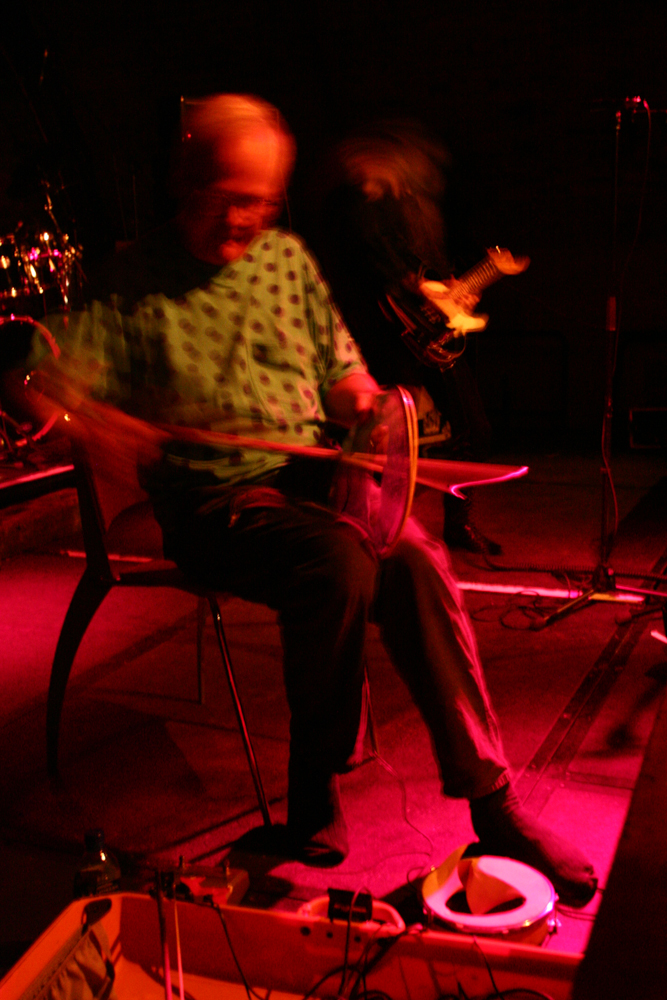 Tony Conrad bowing a torn drum head, Keiji Haino in the background